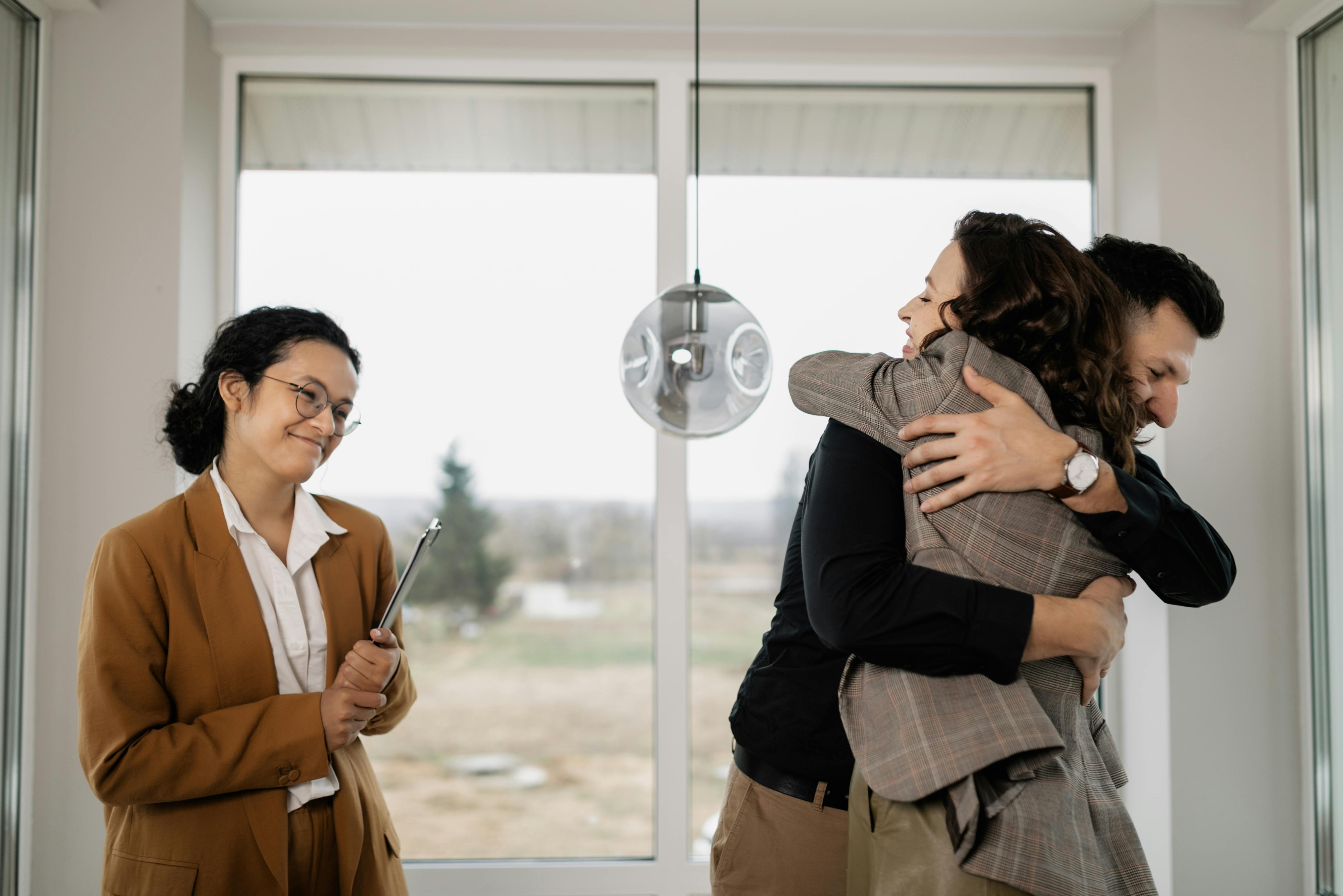 couple hugging and real estate agent looking happy for them